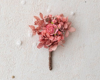 Op de afbeelding: Een klein boeket gedroogde bloemen in roze en witte tinten. Het boeket is vastgebonden met touw en heeft een enkele roze roos in het midden.