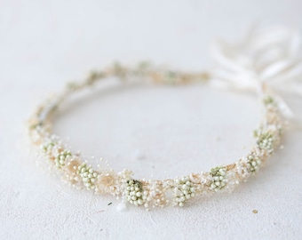Könnte beinhalten: Eine zarte Blumenkrone aus kleinen weißen und grünen Blüten. Die Krone ist aus einem natürlichen Material gefertigt und hat ein schlichtes, elegantes Design.