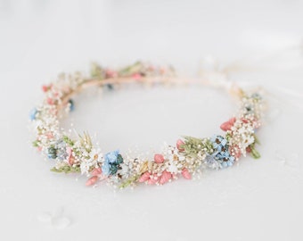 May include: A delicate floral crown made of dried flowers in shades of white, pink, and blue. The crown is made with a wire base and is perfect for a wedding or special occasion.