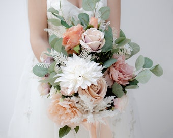 Bouquet de mariée avec des fleurs de soie et des feuilles d’eucalyptus pampa herbe, en rose poussiéreux, pêche, blush, crème. Bouquet de mariage boho et rustique.