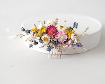 May include: A floral hair comb with dried flowers in shades of pink, yellow, white, and blue. The comb is made of metal and has a gold finish.