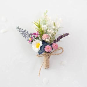 Op de afbeelding: Een klein boeket kunstbloemen gebonden met touw. Het boeket bevat witte, roze en paarse bloemen, evenals groene bladeren.