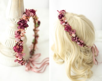 May include: A burgundy and blush floral crown with pink ribbon ties. The crown is made of silk flowers and is perfect for a wedding or special occasion.