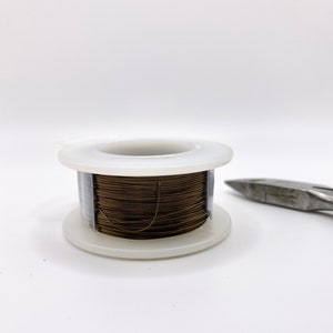 May include: A spool of brown wire wrapped around a white plastic bobbin. The wire is used for crafting and jewelry making.