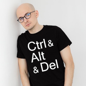 Op de afbeelding: Een man draagt een zwart T-shirt met de tekst "Ctrl & Alt & Del" in wit.