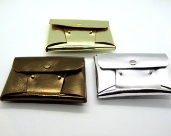 May include: Three small leather wallets in gold, bronze, and silver. Each wallet has a flap closure with a single button.