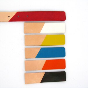 May include: A leather belt with a red painted tip and six color swatches. The swatches are painted in white, yellow, blue, orange, and black. The belt and swatches are on a white background.
