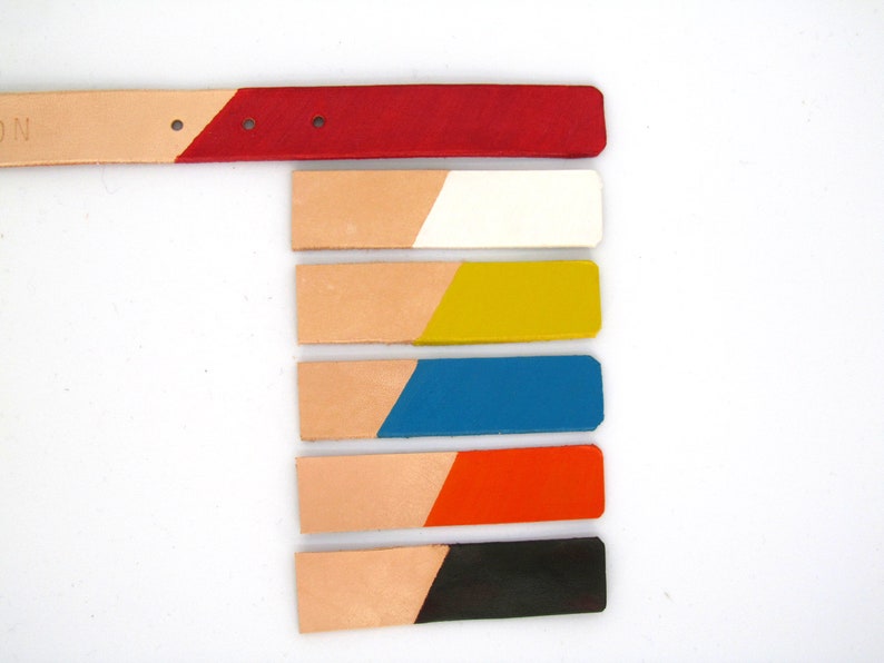 May include: A leather belt with a red painted tip and six color swatches. The swatches are painted in white, yellow, blue, orange, and black. The belt and swatches are on a white background.