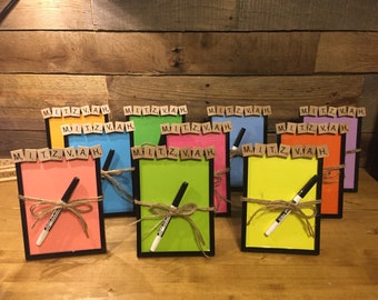 May include: A collection of colorful, framed memo boards with the word "MITZVAH" spelled out in Scrabble tiles. Each board has a black frame, a marker, and is tied with twine. The boards are in various colors.