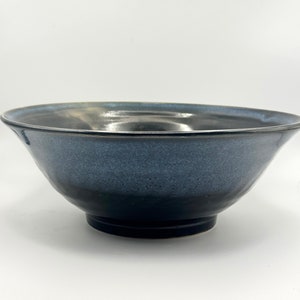 Op de afbeelding: Een grote, donkerblauwe keramische kom met een zwarte rand en bodem. De kom heeft een gespikkeld glazuur en een licht afgeronde vorm.