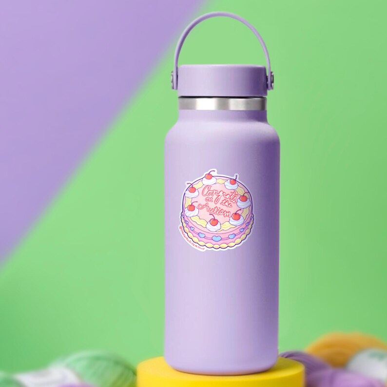 May include: A light purple water bottle with a matching handle and cap. A sticker of a cartoon cake with cherries and the text "Congrats on the occasion" is on the front. The bottle is on a yellow surface with a green and purple background.