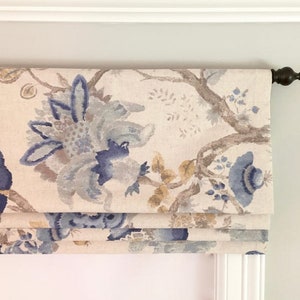 May include: A white roman shade with a blue and brown floral pattern. The shade is raised, showing the fabric folds.