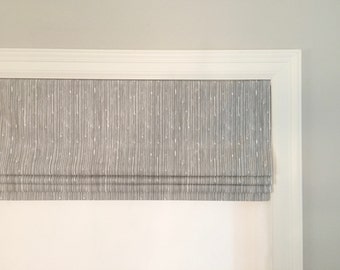 May include: A white window frame with a gray and white patterned roman shade.