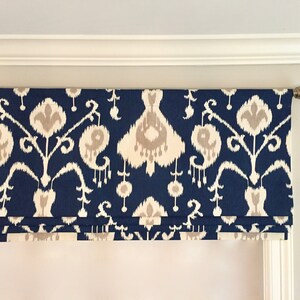 May include: A blue and white patterned valance with a white trim. The valance is hung on a white rod with a gold finial.