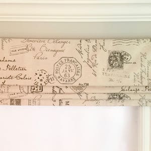 May include: A beige roman shade with a vintage Parisian postmark design. The shade features black text and stamps with French words like "Postes Francaises" and "Par Avion".