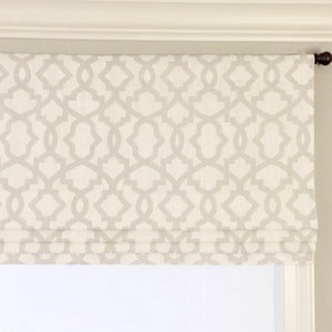 May include: A white roman shade with a geometric pattern in a light gray color. The shade is mounted on a white ceiling.