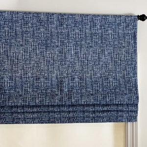 May include: A blue roman shade with a textured fabric. The shade is mounted on a white wall with a black finial.