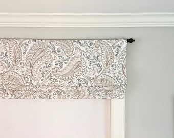 May include: A fabric window valance with a paisley pattern in shades of gray and beige. The valance is mounted on a black rod and hangs above a white window frame. The paisley design is detailed and intricate.