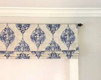 May include: A white roman shade with a blue and white damask pattern. The shade is raised, showing the fabric folds.