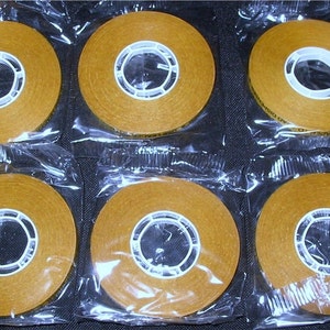 May include: Eight rolls of double-sided adhesive tape, each individually packaged in a clear plastic bag. The tape is brown and has a white core.