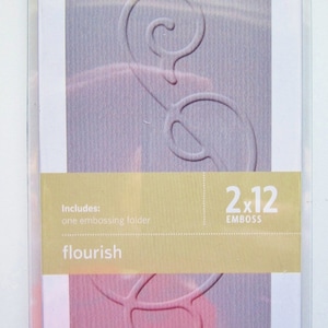May include: A close-up of a 2x12 inch embossing folder with a flourish design. The folder is packaged in a clear plastic sleeve with a gold background and the text "Requires a Quickutz Revolution Tool and a 12-inch Platform" and "Includes: one embossing folder flourish" printed on it.