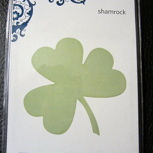May include: A white card with a blue and black floral design in the top left corner. The card says "shamrock" in the top right corner. A green shamrock is in the center of the card. The card says "Quick Kutz" in blue and "Includes: one die" in black at the bottom.