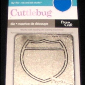 May include: A Cuttlebug die-cutting machine die in a package. The die is in the shape of an Interstate highway sign. The package has the words "Interstate Sign" and "Cuttlebug" printed on it.
