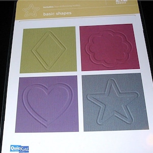 May include: A white card with the text "includes: four embossing folders" and "basic shapes". The card shows four squares with different embossed shapes: a diamond, a flower, a heart, and a star. The squares are in different colors: green, red, purple, and gray.