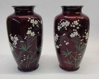 Könnte beinhalten: Zwei rote Cloisonné-Vasen mit weißen Blumenmustern. Die Vasen sind mit weißen Blumen und grünen Blättern verziert.