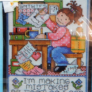 May include: Cross stitch pattern featuring a cartoon woman sitting at a desk with a calendar, coffee cup, and papers. The text "USH Me!!!" is above the woman and the text "I'm making mistakes as fast as I can" is below the woman.