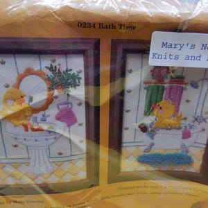 May include: Two framed cross-stitch embroidery patterns, one depicting a yellow duck taking a bath and the other a duck in a bathtub. The title of the pattern is "0234 Bath Time" and the company name is "Mary's Neat Knits and Kits".