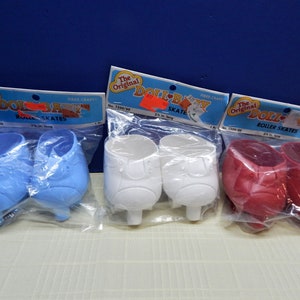May include: Three pairs of doll roller skates in blue, white, and red, each packaged in clear plastic. The packaging includes a header card with the text "The Original Doll-Baby Roller Skates". Each pair measures 2.5 inches in length.