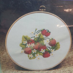 May include: Embroidered hoop art featuring a cluster of red strawberries with green leaves and white flowers.