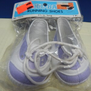 May include: A pair of doll-sized running shoes in a clear plastic package. The shoes are white with lavender accents and white laces. The packaging includes the text "DOLL BAG RUNNING SHOES" and the length of the shoes is 2.5 inches.