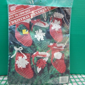 May include: A package of Banar Designs Christmas ornaments. The package contains six crocheted mini stockings in red and green, with white snowflake and floral accents. The package text reads "Fun to Crochet Christmas Ornaments".