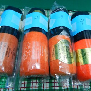 May include: Four spools of yarn in clear plastic packaging. The yarn is primarily orange with black or green accents. Each spool has a blue label with a number. The packaging includes text from "Pretty Punch Shoppelles, Inc."