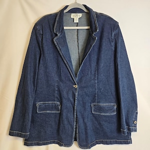 Könnte beinhalten: Ein dunkelblauer Jeansblazer mit einem Knopfverschluss, fallendem Revers und zwei Vordertaschen mit Klappen. Die Jacke hat lange Ärmel mit jeweils einem Knopf an den Manschetten und ein sichtbares Markenetikett am inneren Halsausschnitt.