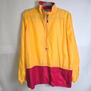 May include: A yellow and red windbreaker jacket with a half-zip closure. The jacket has a stand-up collar with a red lining and a small pocket on the lower front. The jacket is hanging on a gray hanger.