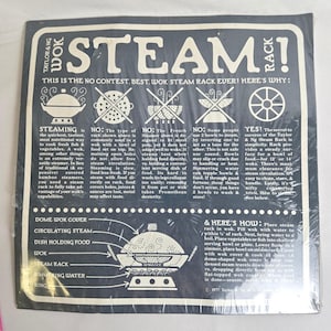 May include: A black and white Taylor & Ng Wok Steam Rack package. The package features text and diagrams explaining the benefits of steaming food in a wok, with instructions and warnings.