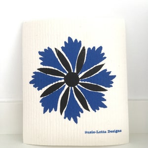 Peut inclure: Un torchon en coton blanc avec un motif de fleur stylisé bleu et noir. Le texte "Susie-Lotta Designs" est imprimé dans le coin inférieur droit.