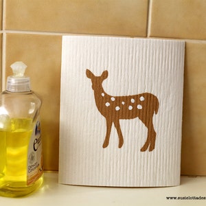 Peut inclure: Une éponge de cuisine blanche avec une silhouette de cerf brune imprimée dessus. Le cerf a des taches blanches et se tient sur un fond blanc.