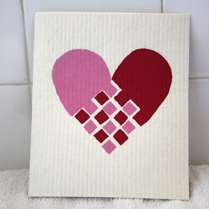 Peut inclure: Un torchon blanc avec un motif de cœur rose et rouge. Le cœur est composé d'une grille de carrés.