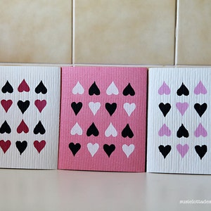 Peut inclure: Trois torchons de cuisine avec un motif de cœurs. Les torchons sont blancs, roses et blancs avec des cœurs noirs, blancs et roses.