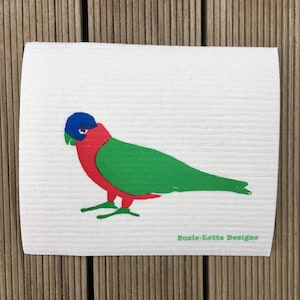 May include: A white, rectangular cleaning cloth featuring a colorful illustration of a bird. The bird has a blue head, red chest, green wings, and green feet. The text "Susie-Lotta Designs" is printed in green on the bottom right corner.