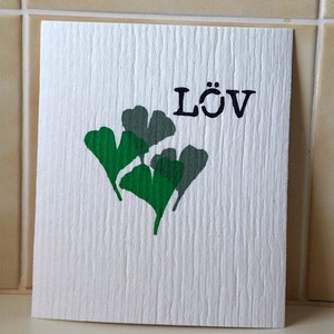 Peut inclure: Une carte blanche avec un motif de feuille de ginkgo vert et gris et le mot "LÖV" imprimé en noir.