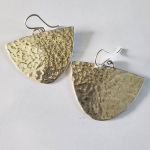 May include: A pair of gold-toned hammered metal earrings with a crescent shape. The earrings have a textured surface and a simple hook closure.