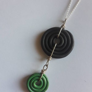 May include: A black and green necklace with two circular pendants. The top pendant is black and has concentric circles. The bottom pendant is green and has concentric circles.
