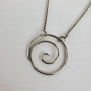 May include: A silver necklace with a spiral pendant. The pendant is made of a single piece of wire that is twisted into a spiral shape. The necklace is on a silver chain.