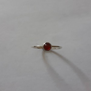 May include: A silver ring with a small, round, red gemstone.