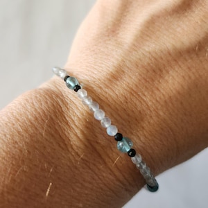 May include: A beaded bracelet with white, blue, and black beads. The bracelet is on a person's wrist.